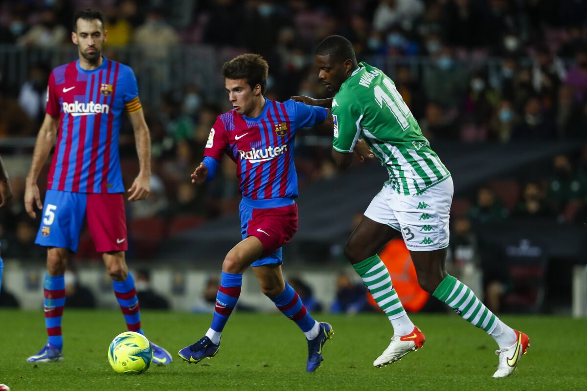 Barcelona's Riqui Puig, center, vies for the ball with Betis' William Carvalho during the Spanish La Liga soccer match between Barcelona and Real Betis at the Camp Nou stadium, in Barcelona, Spain, Saturday, Dec. 4, 2021. (AP Photo/Joan Monfort)