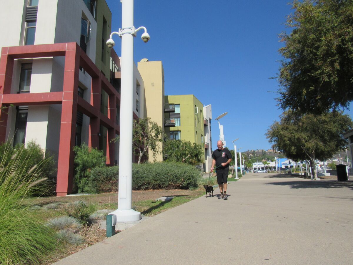 A man and his dog walk by a pole with two cameras attached to it in Promenade Park in Lemon Grove.
