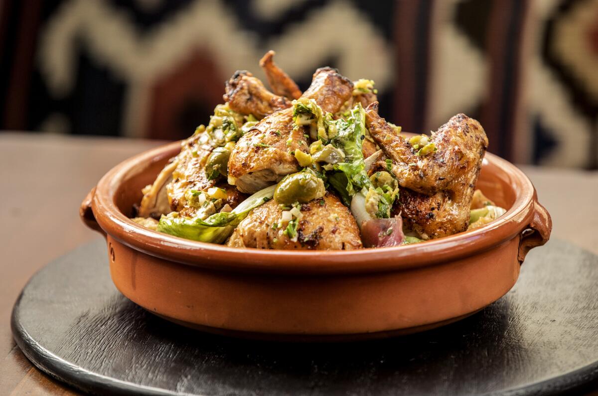 A clay, high-rimmed dish is piled with chicken, panzanella, fennel and green olives.