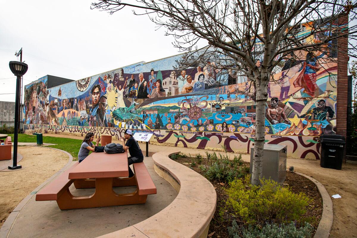 People sit at a picnic table in front of a large colorful mural.