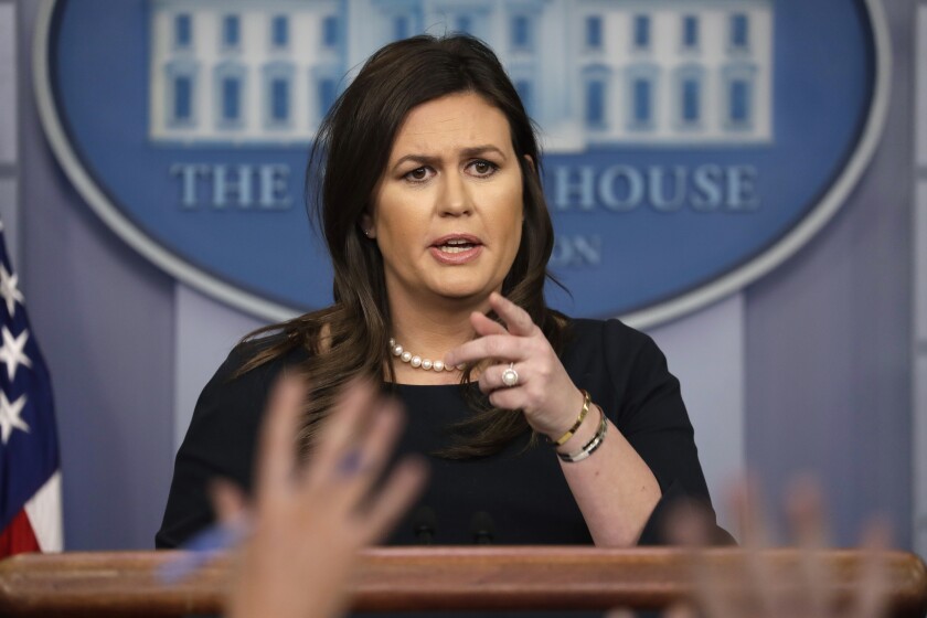 Sarah Huckabee Sanders speaks during a news briefing at the White House while hands are raised in front of her.