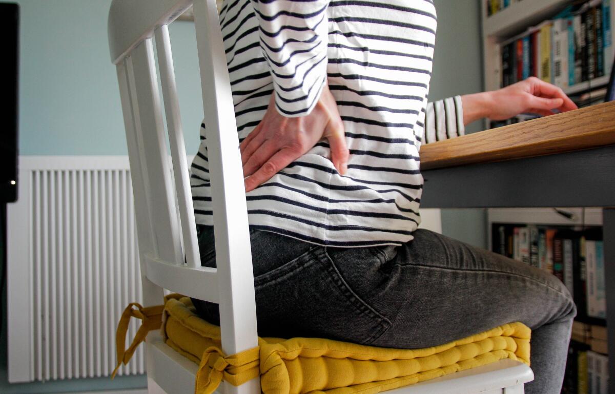 A person sitting in a chair experiences lower back pain.