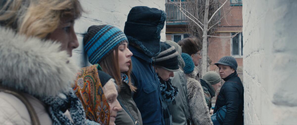 People wearing cold-weather clothes line up in war-ravaged eastern Ukraine in the movie "Donbass."