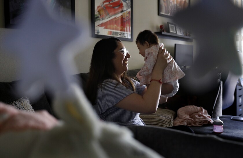 Η Veronica Gutierrez κάθεται σε έναν καναπέ και κρατά την 3 μηνών κόρη της, Alessandra. 