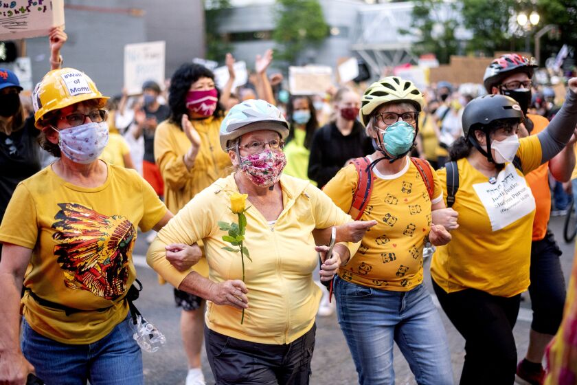 Norma Lewis holds a flower while forming a "wall of moms" during a Black Lives Matter protest in Portland, Ore. on July 20, 2020. (AP Photo/Noah Berger)