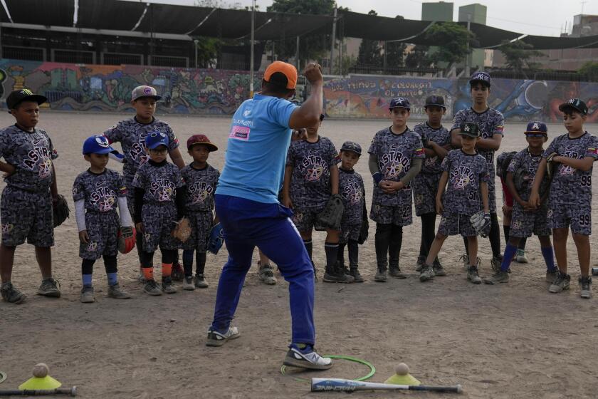 Baseball coach Franklin Lopez shows young Venezuelan migrants how to throw a ball during a baseball practice session in a public park in the Comas area, on the outskirts of Lima, Peru, Thursday, May 2, 2024. Immigrants, mainly Venezuelans, have opened five baseball academies in Peru's capital. (AP Photo/Martin Mejia)