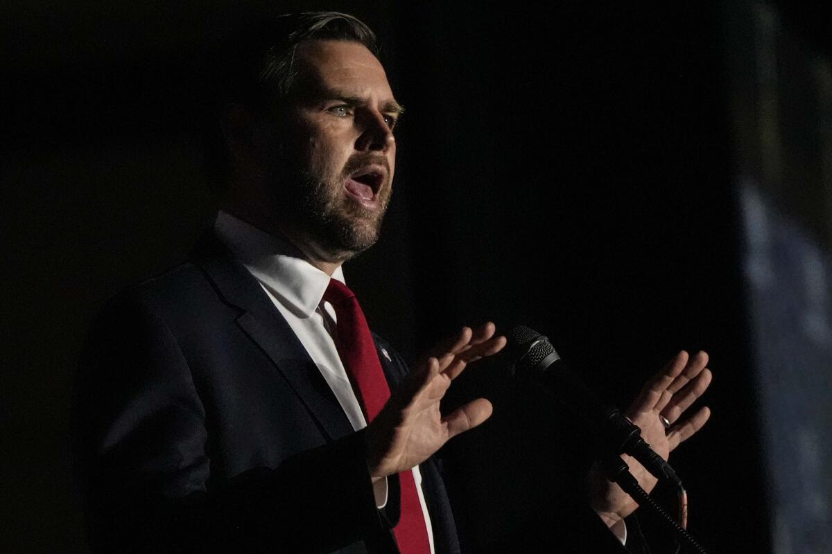 JD Vance speaking and gesturing with both hands, at a mic 