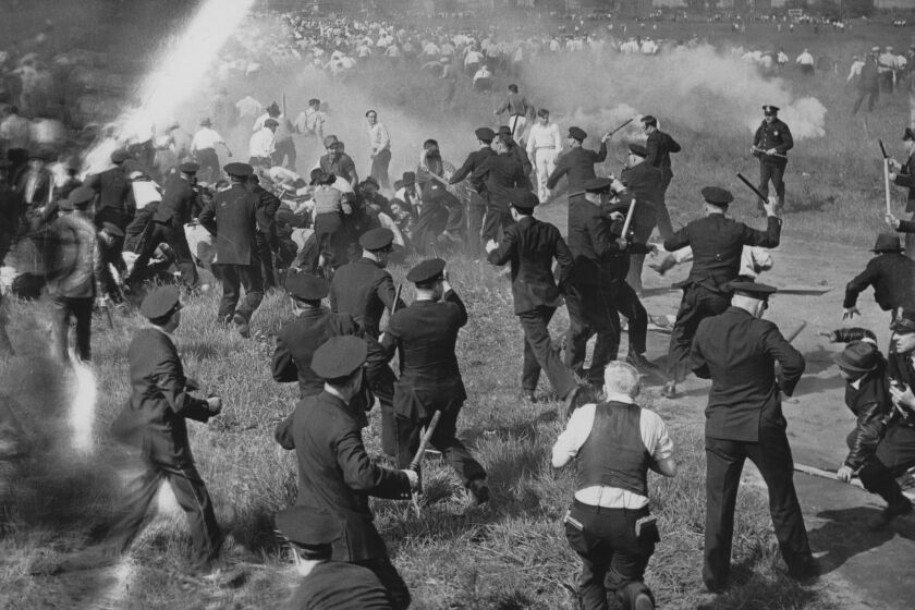 A black-and-white frame of a crowd of police officers confronting strikers - beating them with clubs