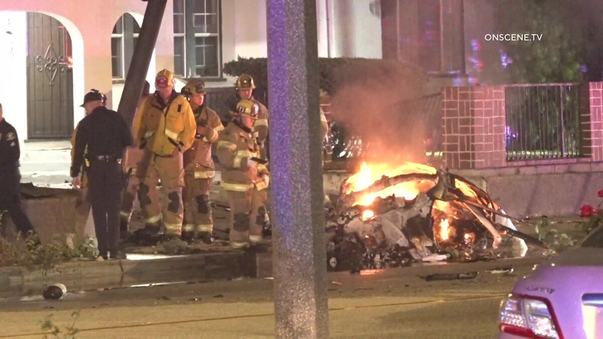 Firefighters and police stand near a burning car