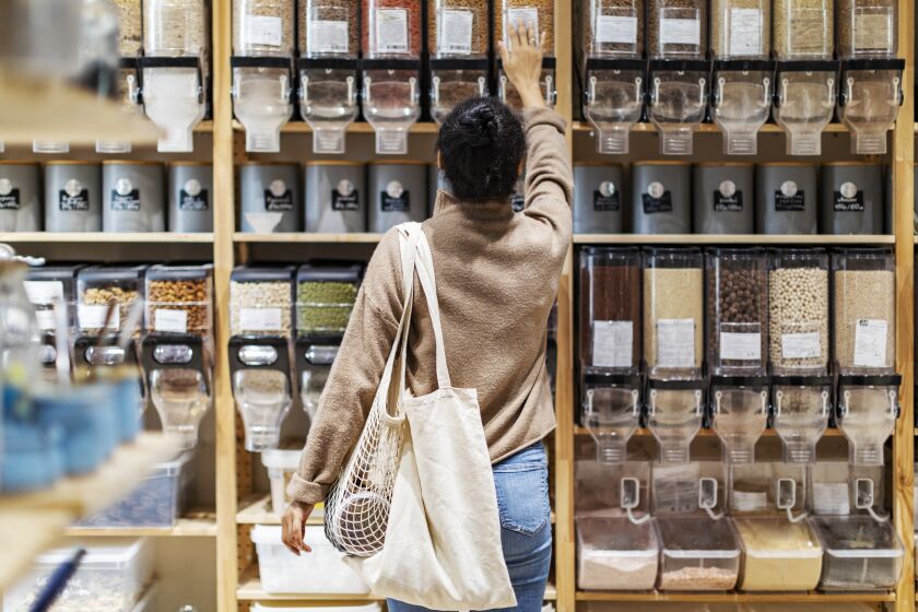 Young woman with tote bags shops for groceries in a zero waste store.