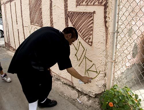 A Florencia 13 gang member sprays graffiti on a garage in Florence-Firestone, an unincorporated neighborhood north of Watts.