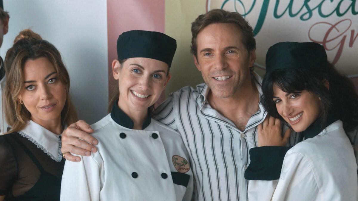Three women and a man stand together, smiling, for a photo. Two women wear chef's uniforms.