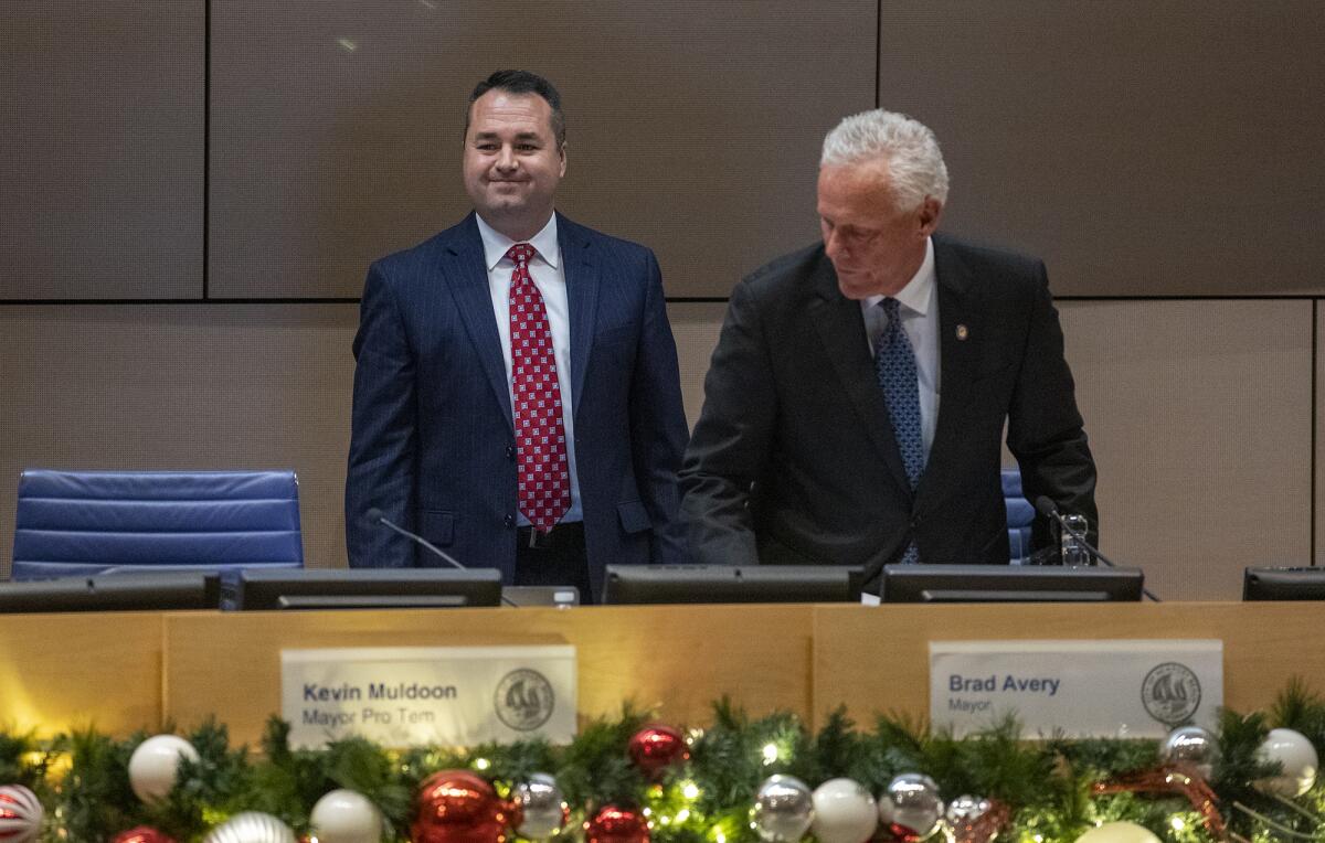 Incoming Mayor Kevin Muldoon, left, switches seats with outgoing Mayor Brad Avery.