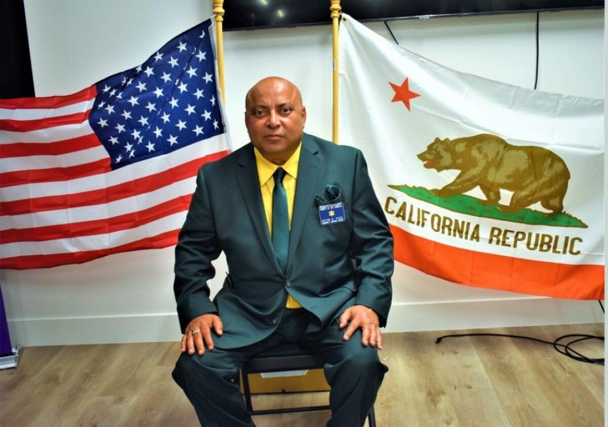 A man seated in front of California and U.S. flags