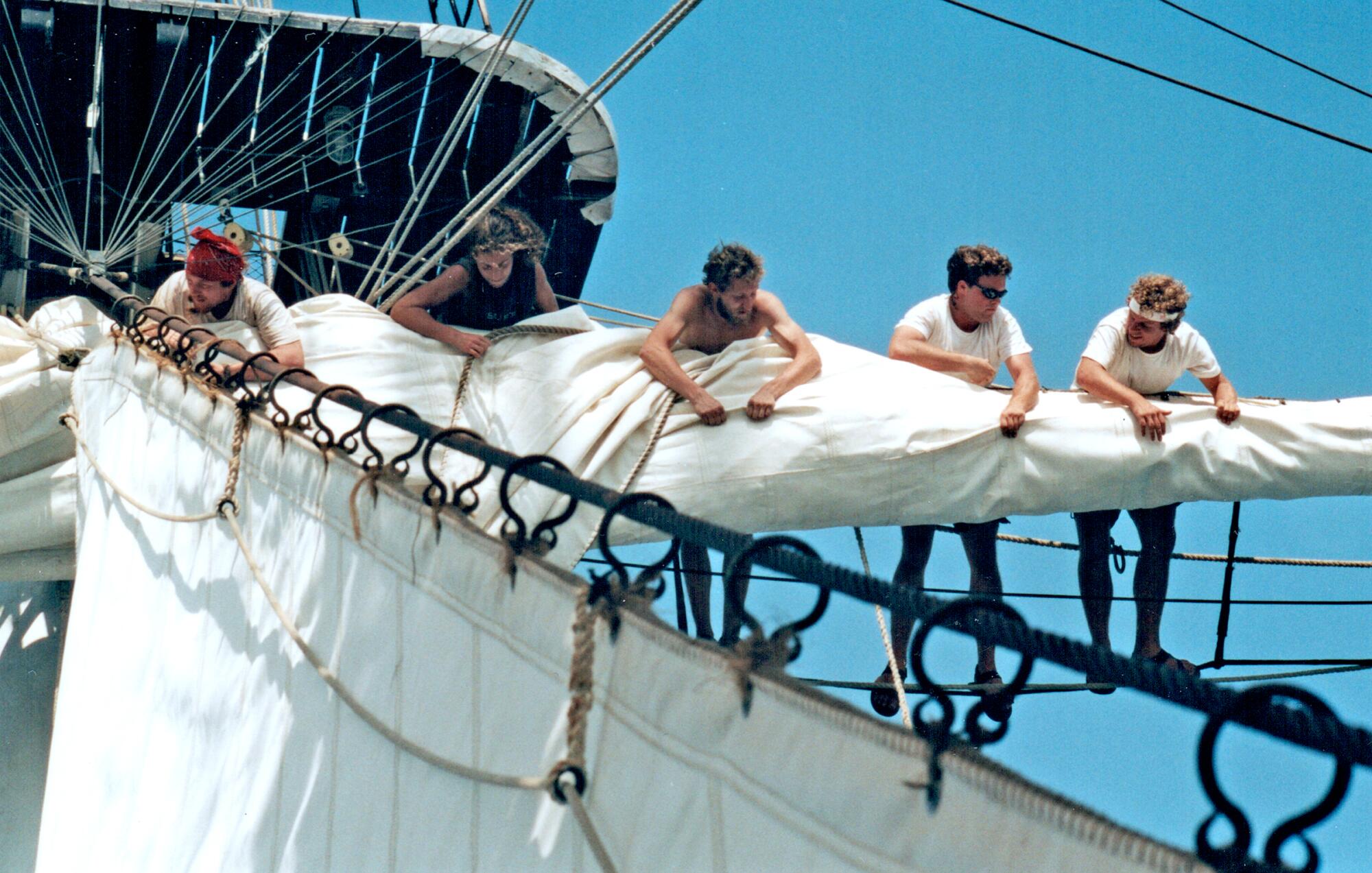 Crew members stand in the tall ship's rigging.