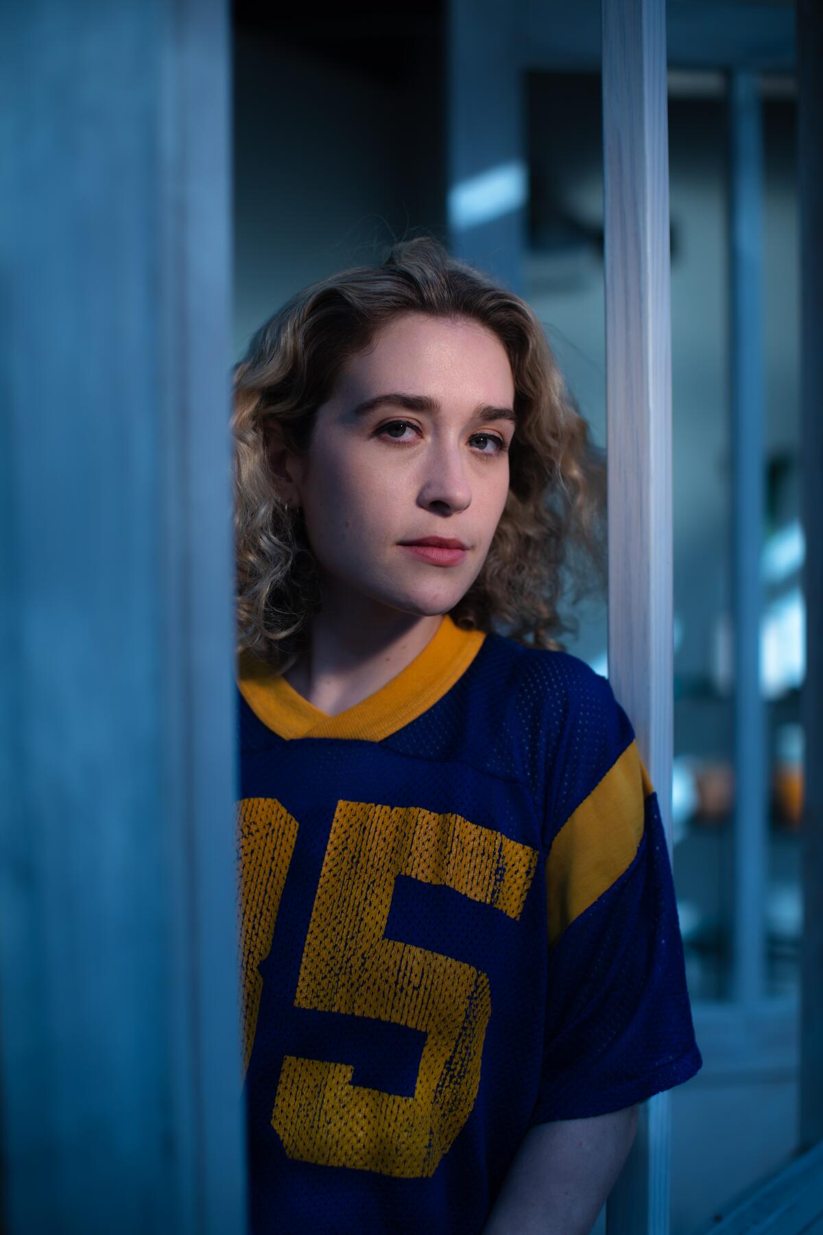 A woman in a football jersey peers out from behind a doorway