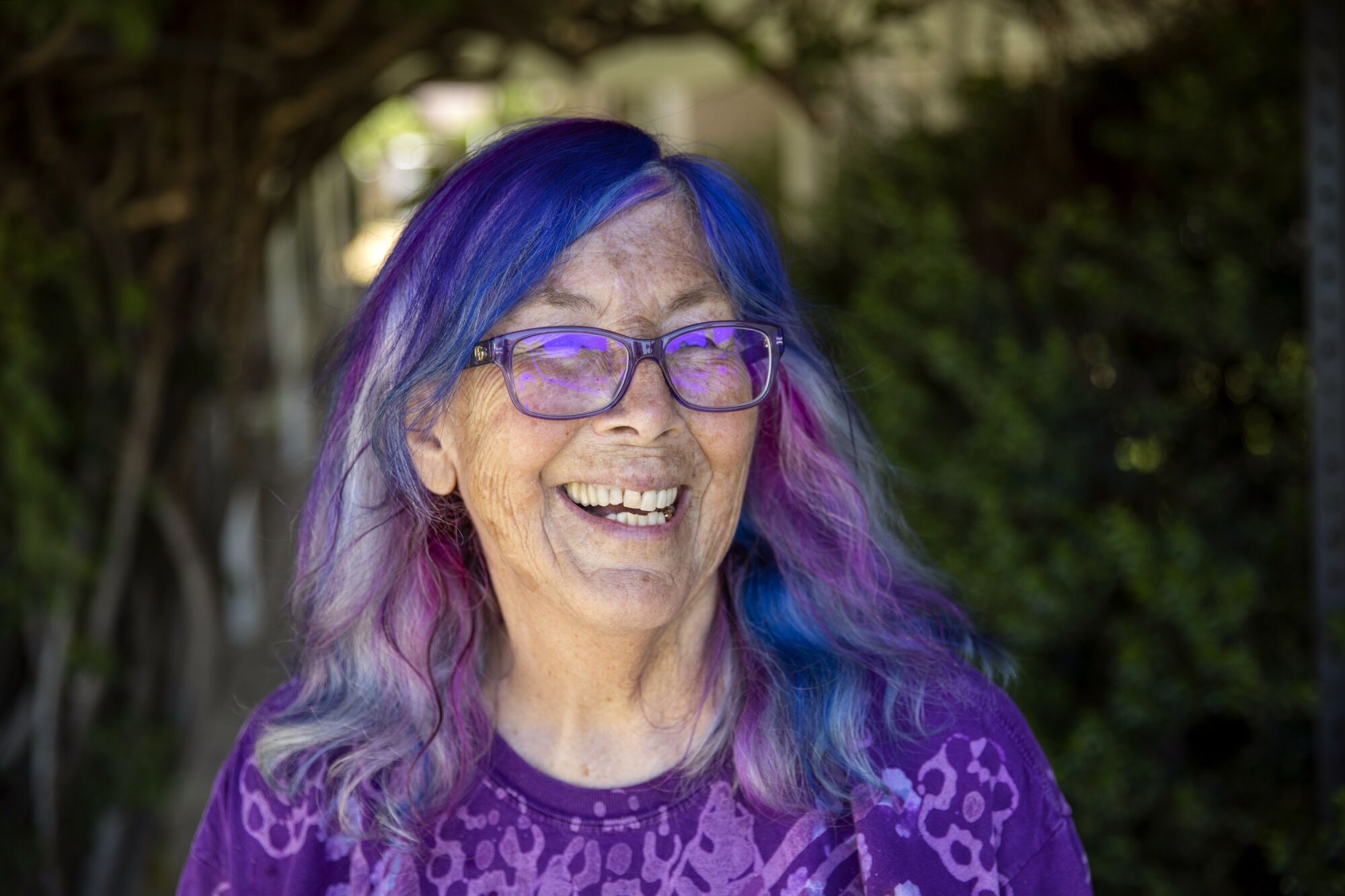 A smiling woman with purple hair, wearing a purple shirt.
