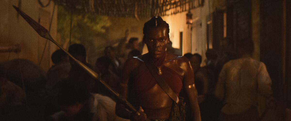 A woman on a crowded street holds a spear and looks fierce.
