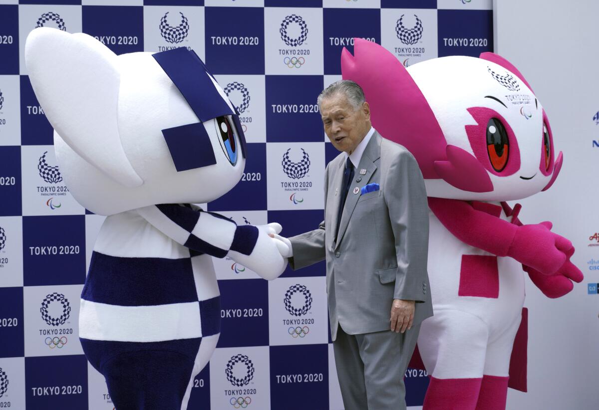 A man in a suit and tie shakes the hand of one of two people in mascot costumes.