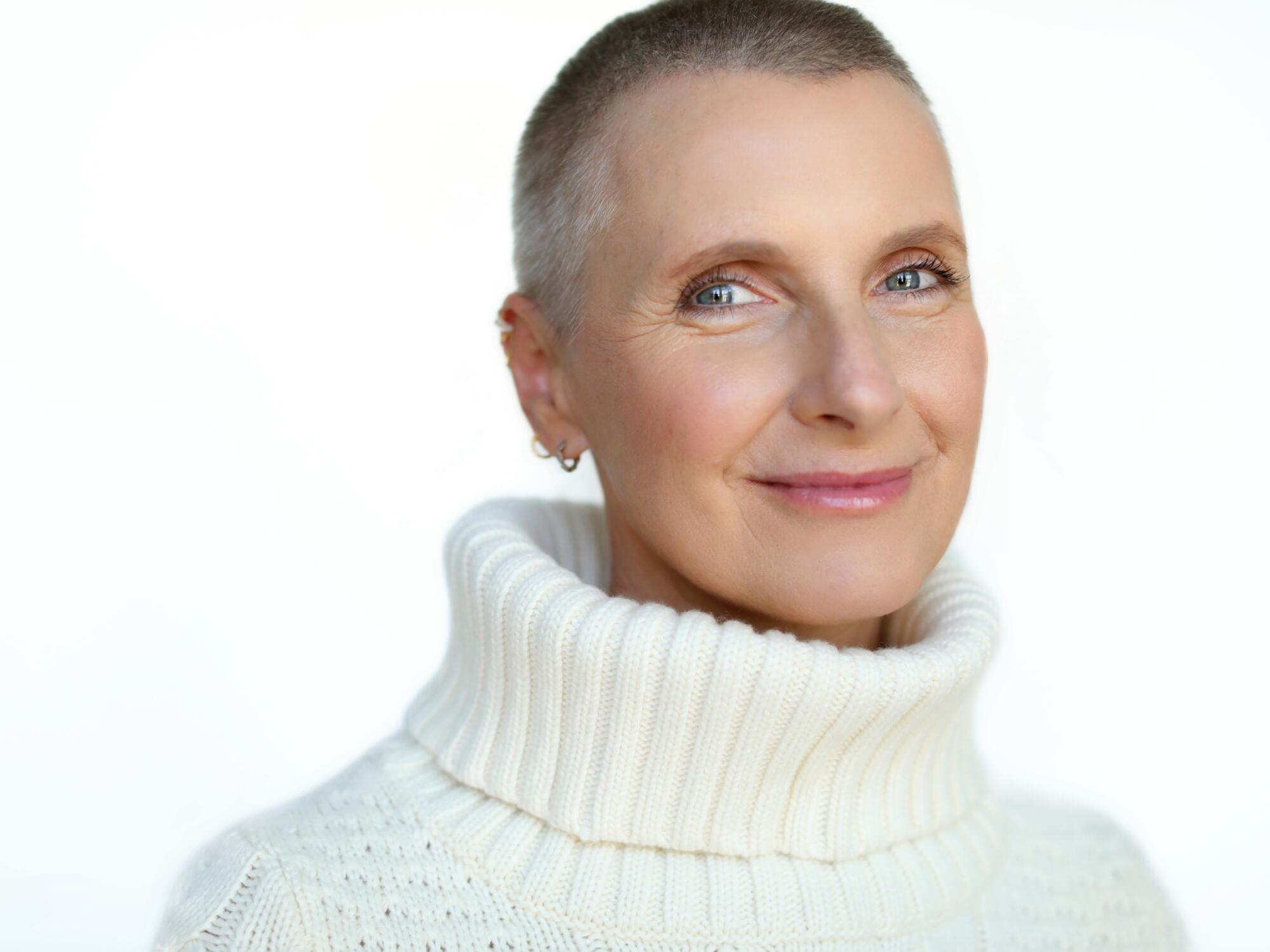 Elizabeth Gilbert, with short hair and a white turtle-neck cable-knit sweater, smiles at the camera.