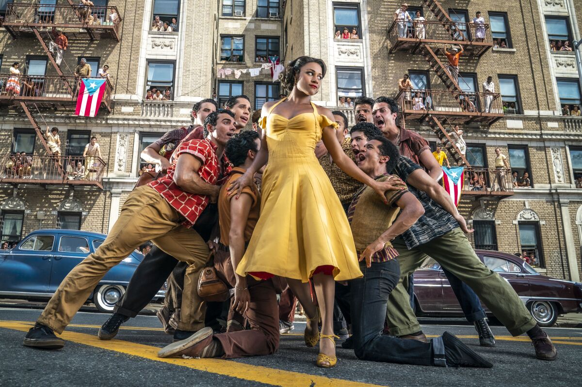 A cluster of men lean into a woman in a yellow dress in "West Side Story."