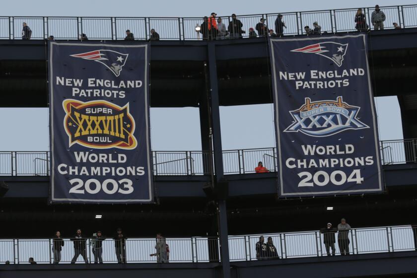 Fans stand on the upper decks of Gillette Stadium behind three New England Patriots Super Bowl banners.