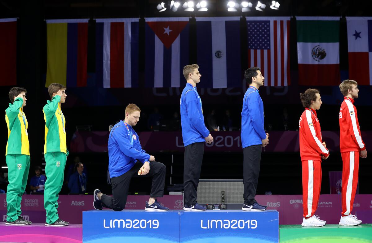U.S. fencer Race Imboden kneels on the podium during the men's team foil medal ceremony