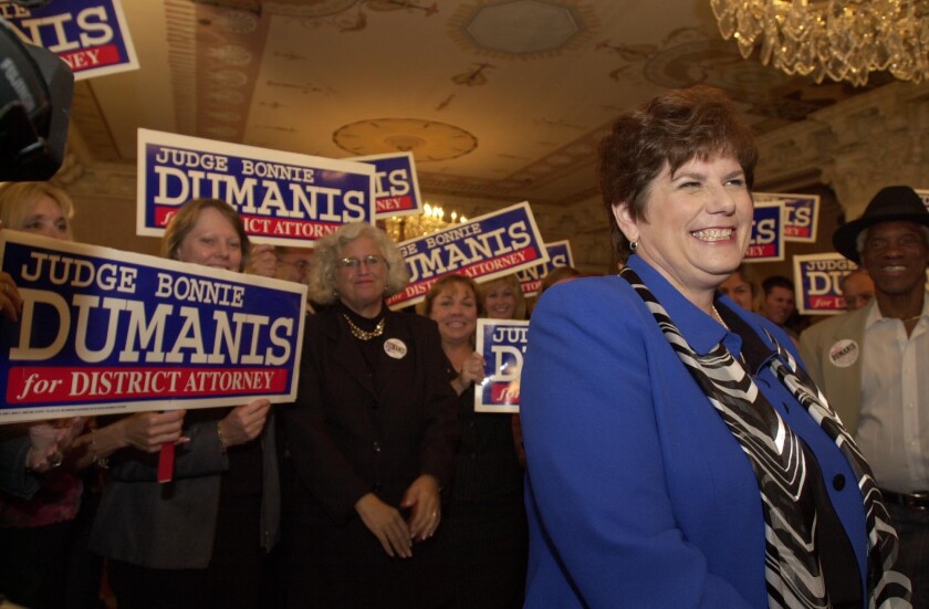 A smiling woman stands in front of a crowd of supporters holding signs that say "Judge Bonnie Dumanis for District Attorney"