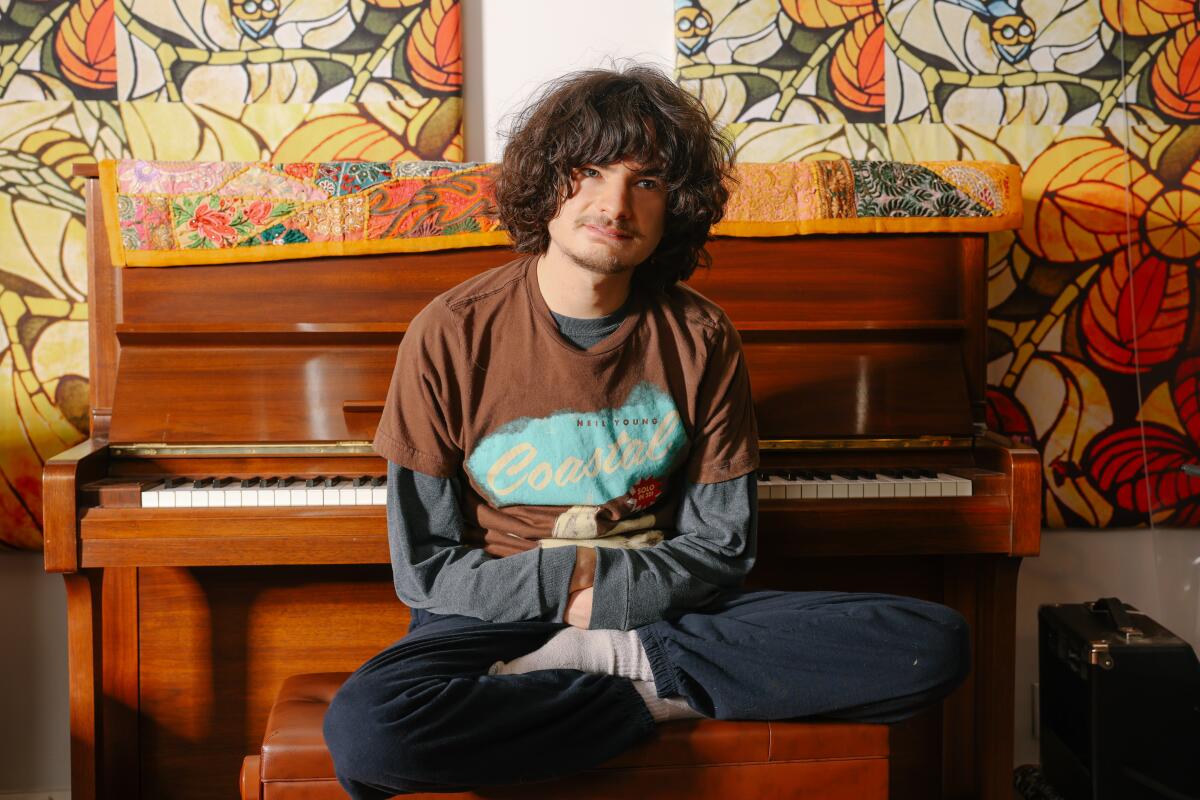 A teenager with long curly hair sits in front of a piano