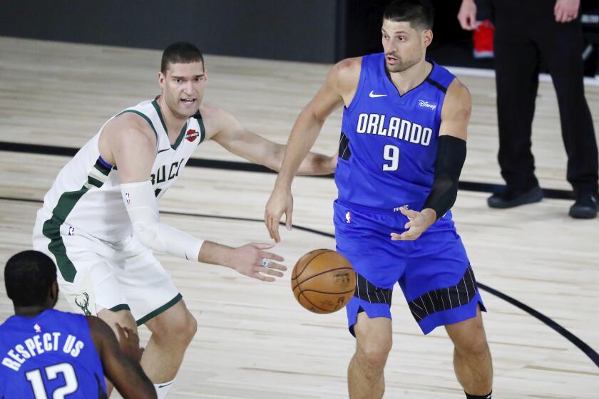 Orlando Magic center Nikola Vucevic (9) passes the ball to forward Gary Clark (12) in front of Milwaukee Bucks center Brook Lopez (11) during the first half of Game 1 of an NBA basketball first-round playoff series, Tuesday, Aug. 18, 2020, in Lake Buena Vista, Fla. (Kim Klement/Pool Photo via AP)
