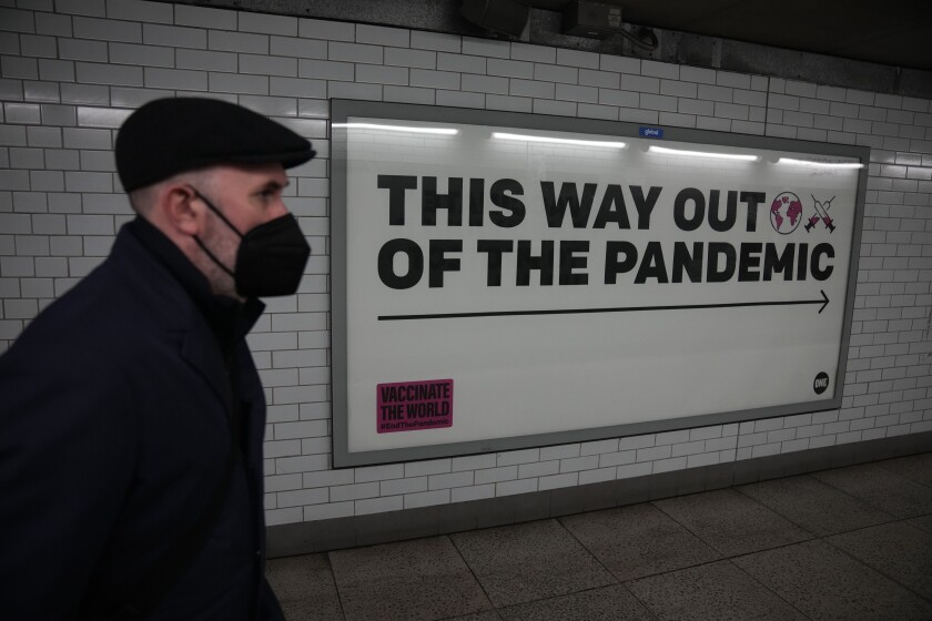 A man wearing a face mask to curb the spread of coronavirus walks past a health campaign poster from the One NGO, in an underpass leading to Westminster underground train station, in London, Thursday, Jan. 27, 2022. Most coronavirus restrictions including mandatory face masks were lifted in England on Thursday, after Britain's government said its vaccine booster rollout successfully reduced serious illness and COVID-19 hospitalizations. From Thursday, face coverings are no longer required by law anywhere in England. (AP Photo/Matt Dunham)