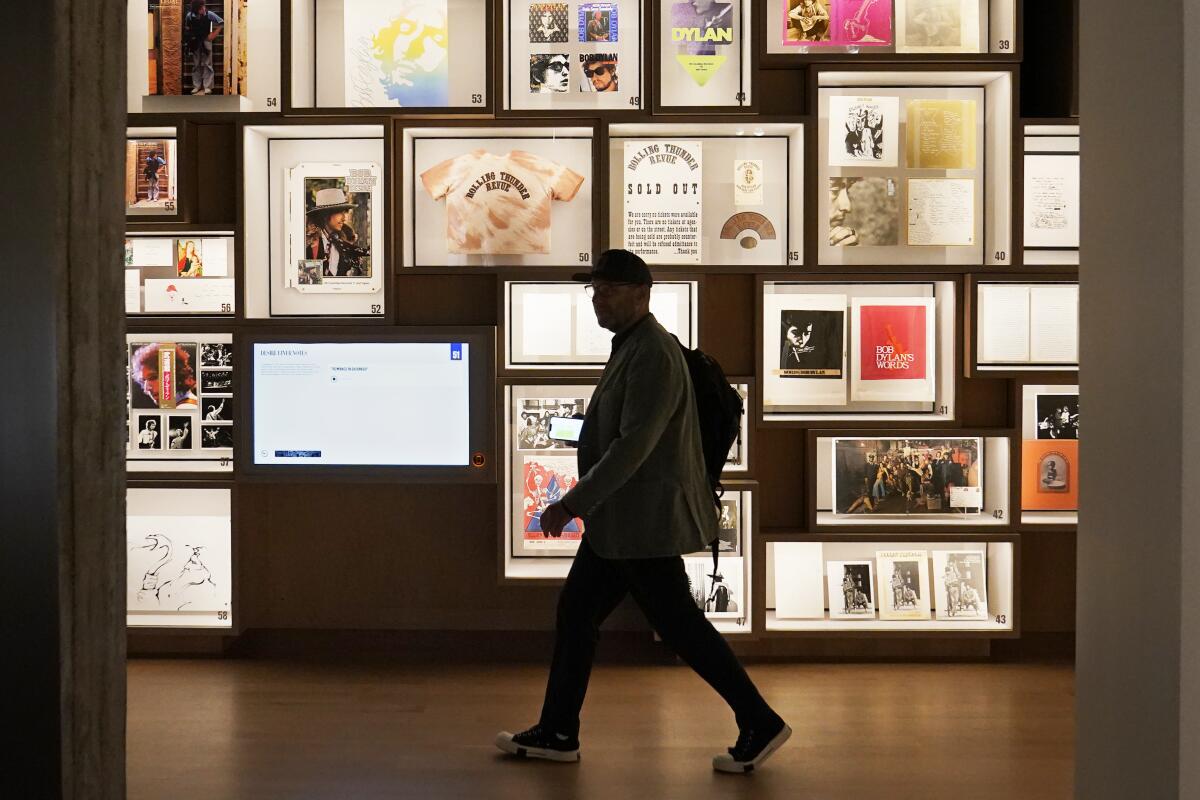 A man walks past a portion of the archive wall at the Bob Dylan Center, Thursday, May 5, 2022, in Tulsa, Okla. The center offers an immersive film experience, performance space, a studio where visitors can play producer and "mix" different elements of instrumentation in Dylan's songs and a curated tour where people can take a musical journey through the stages of his career. (AP Photo/Sue Ogrocki)