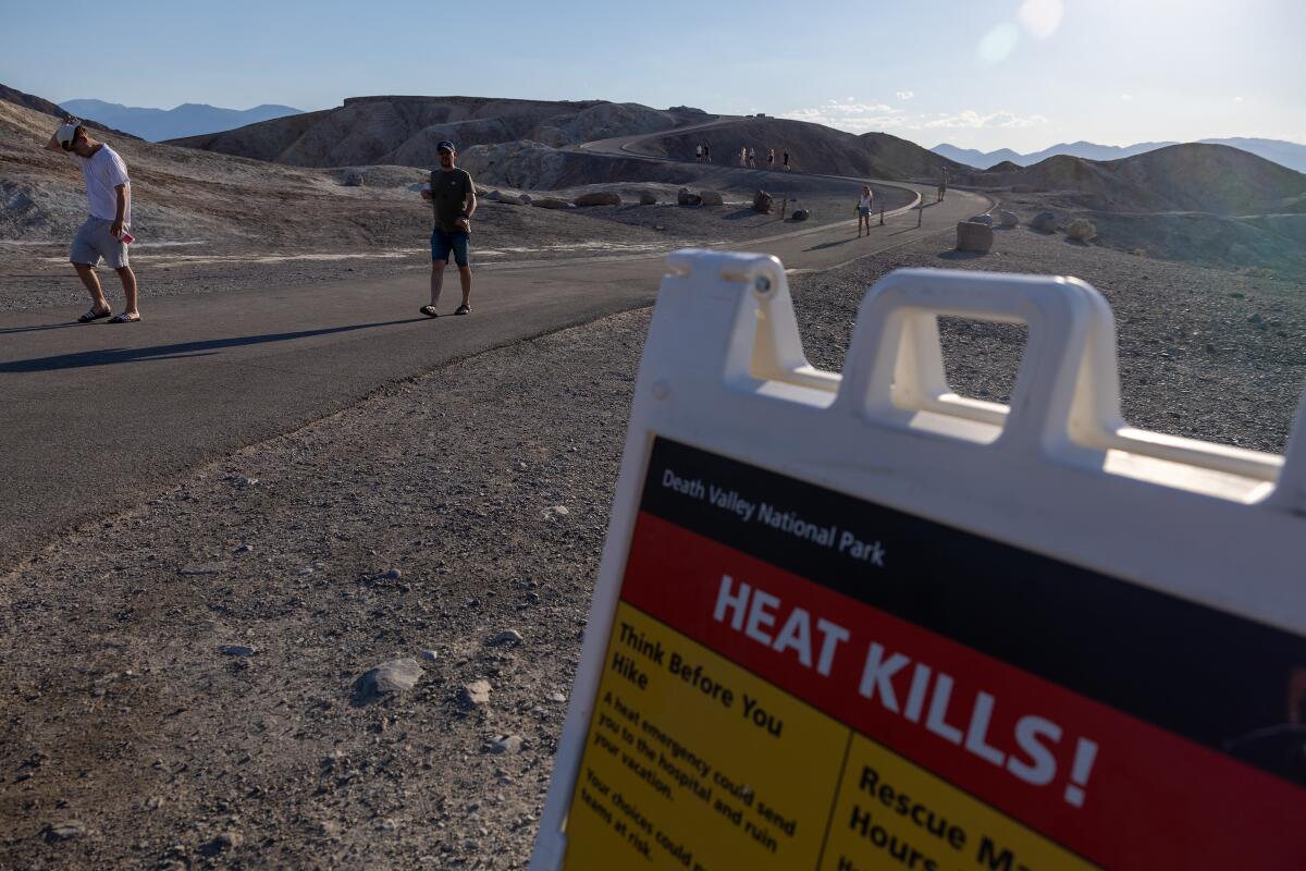 Visitors walk in Death Valley near a sign reading "Heat Kills!"