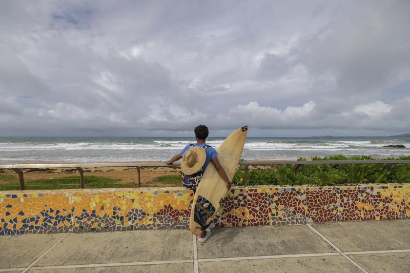 Un surfista se prepara para entrar en el agua antes del paso de la tormenta tropical Ernesto en la playa de La Pared en Luquillo, Puerto Rico, el martes 13 de agosto de 2024. (AP Foto/Alejandro Granadillo)