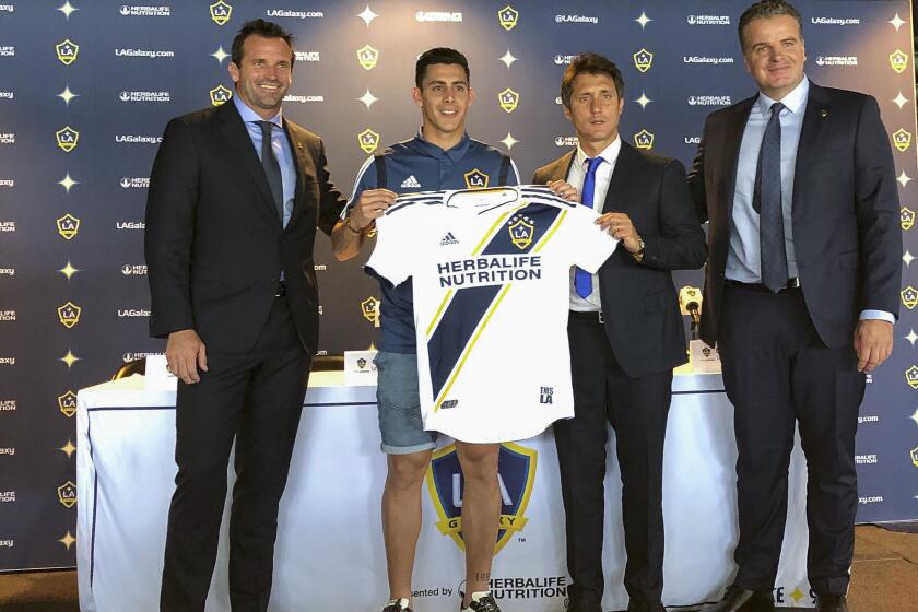 Forward Cristian Pavón, middle, of Argentina, holds up his new LA Galaxy jersey at Dignity Health Sports Park in Carson, Calif., Thursday, Aug. 8, 2019. Standing alongside Pavon, left to right, Galaxy President Chris Klein, head coach Guillermo Barros Schelotto and general manager, Dennis te Kloese. The LA Galaxy acquired Pavón on loan from Argentina's Boca Juniors this week in one of the biggest player acquisitions in recent Major League Soccer history. (AP Photo/Greg Beacham)
