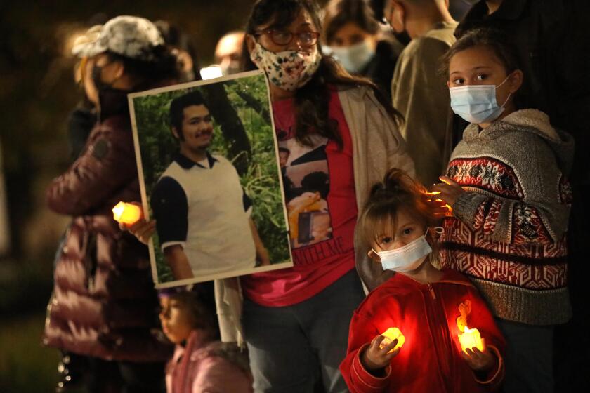 LOS ANGELES, CA - DECEMBER 31, 2020 - Mary Smay holds a photo of her murdered son Juan Vidal, while Vidal's nieces Amaya Rivera, 3, and Alia Rivera, 8, right, join other family and community members at a candlelight vigil for victims of a violent crime and to ensure access to justice at the Hall of Justice in downtown Los Angeles on December 31, 2020. Vidal was murdered in October 21, 2016. Family members who have endured the crime of murder spoke along with two concerned Deputy District Attorneys, Jon Hatami and John McKinney. Family members were demanding fair access to justice from newly elected District Attorney George Gascon. The protest was organized by the Recall George Gascon Facebook community. Los Angeles on Thursday, Dec. 31, 2020 Los Angeles, CA. (Genaro Molina / Los Angeles Times)