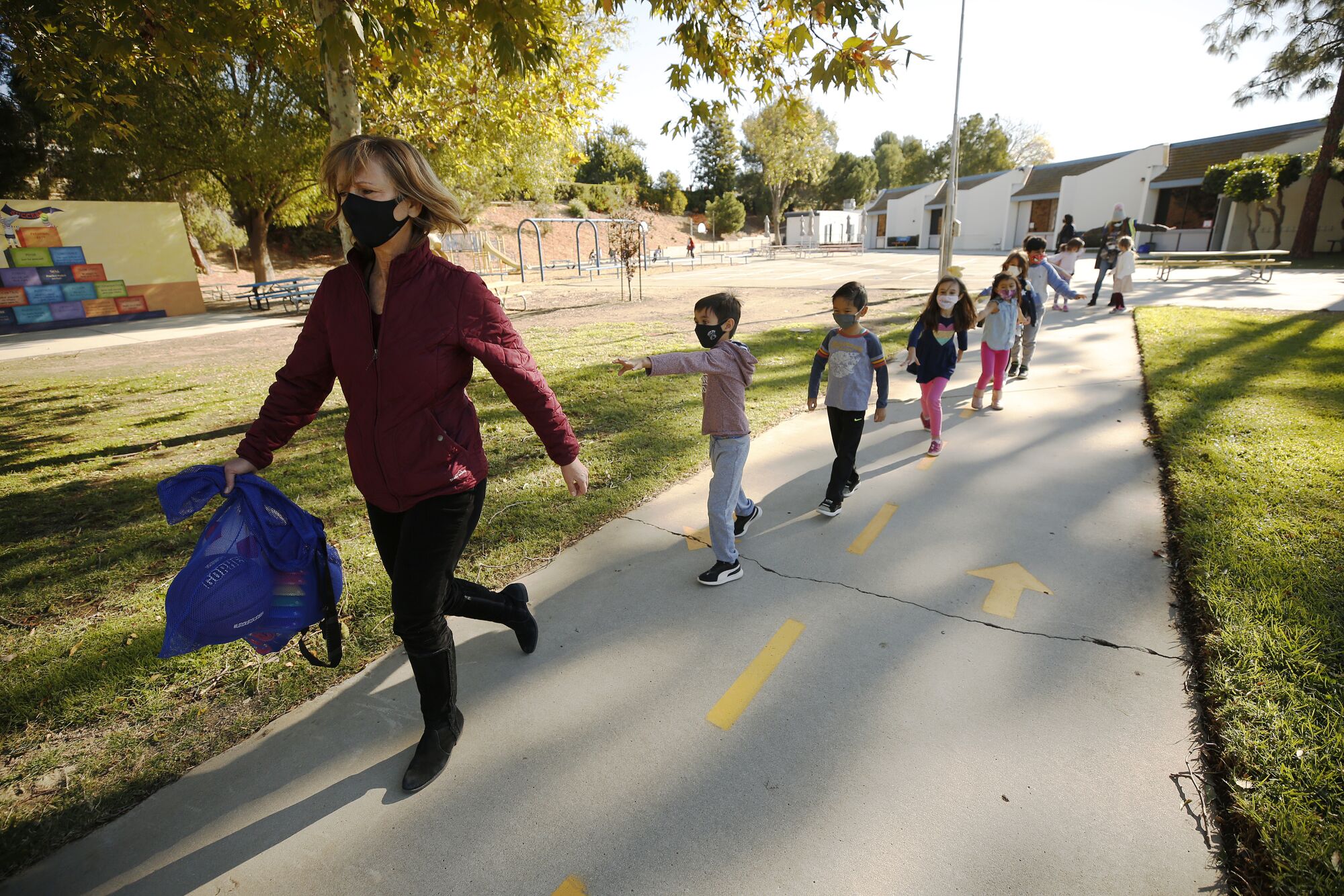 Jennifer Klein leads a line of masked students along a pathway at Lupin Hill Elementary.