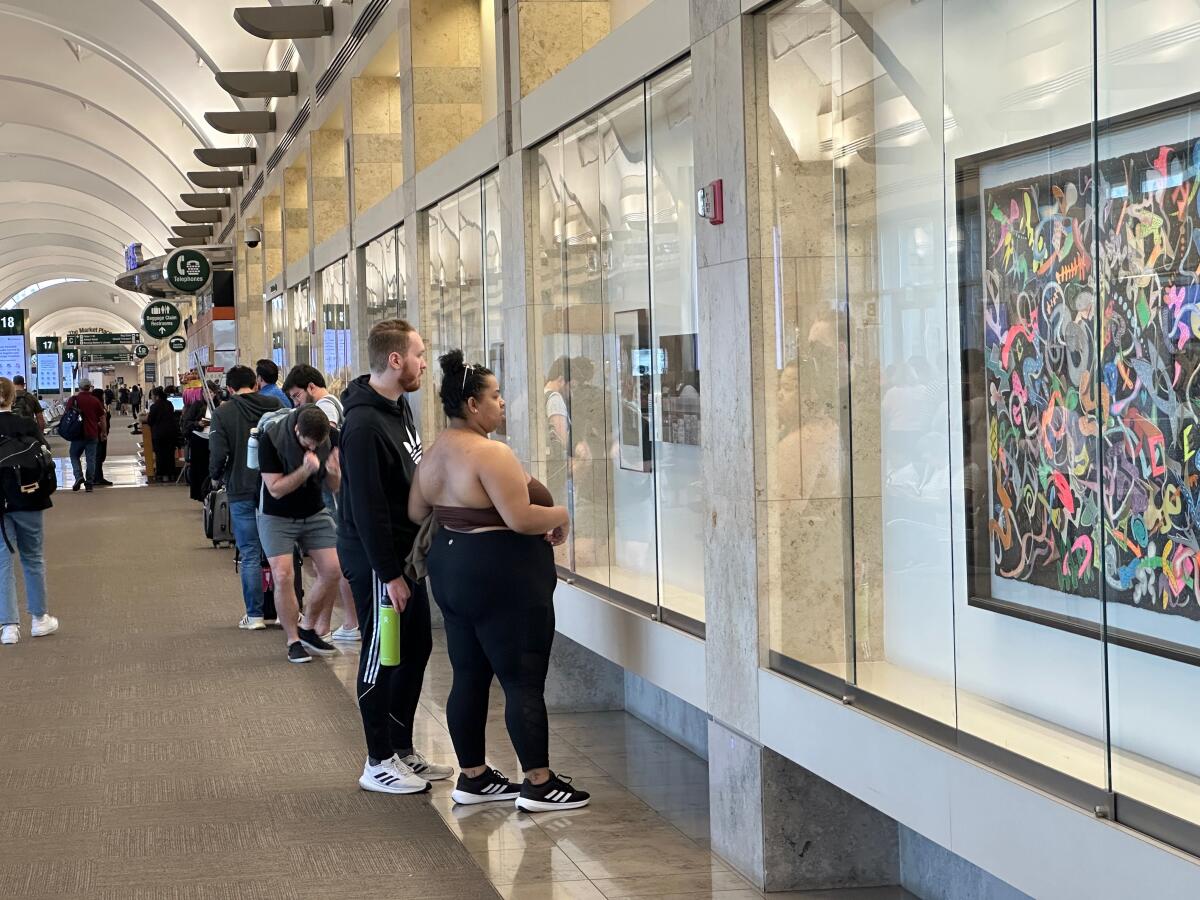 Travelers take in the artwork on display in a Festival of Arts permanent collection exhibit at John Wayne Airport.