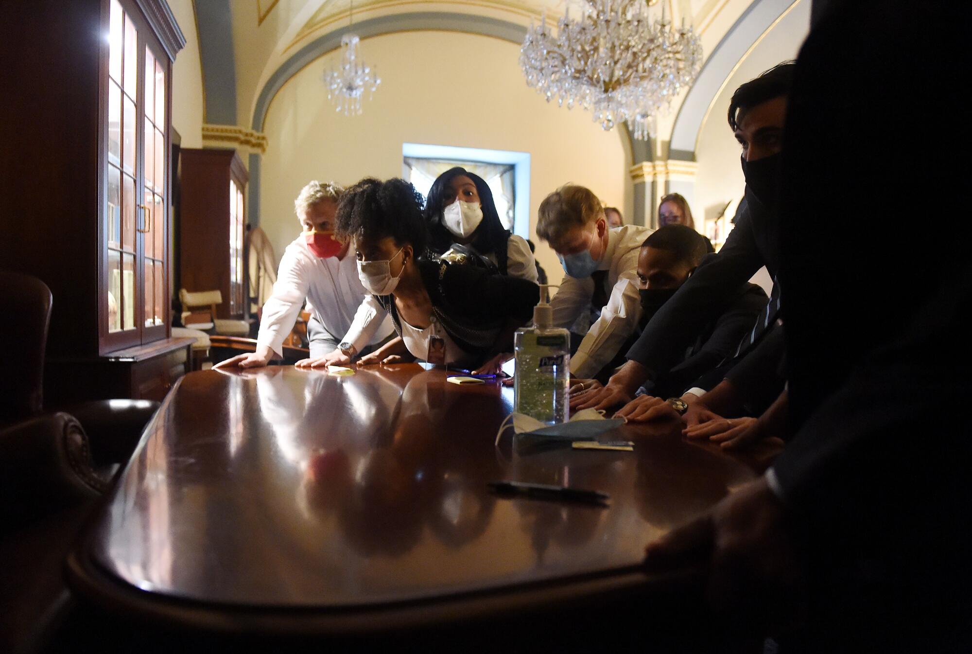 Congressional staffers in masks lean into a piece of furniture, pushing it to toward a door.