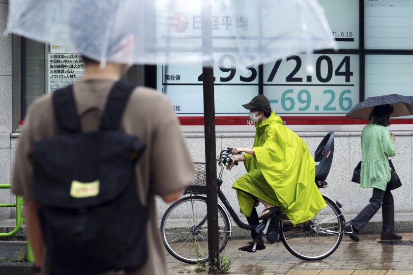 A person wearing a protective mask rides a bicycle in front of an electronic stock board showing Japan's Nikkei 225 index at a securities firm in the rain Wednesday, June 16, 2021, in Tokyo. Asian shares were mixed in quiet trading Wednesday ahead of a U.S. Federal Reserve meeting that may give clues on what lies ahead with its massive support for markets. (AP Photo/Eugene Hoshiko)