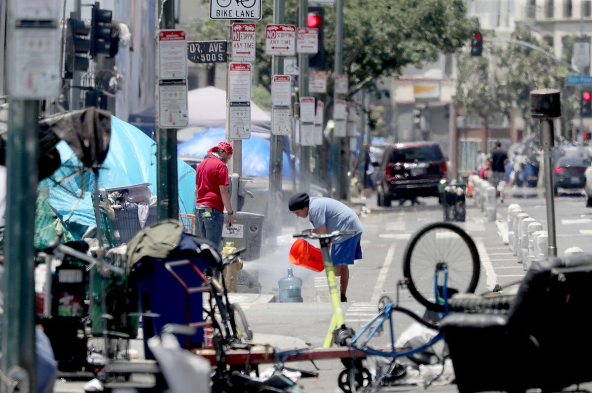 Unhoused people by an encampment on a street draw water from a hydrant.