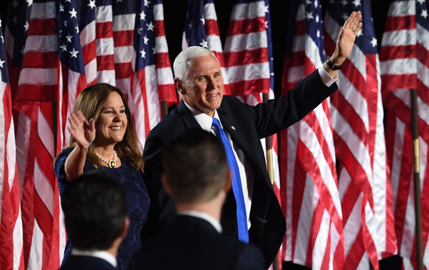 Vice President Mike Pence and Second Lady Karen Pence wave from the stage in front of a backdrop of U.S. flags