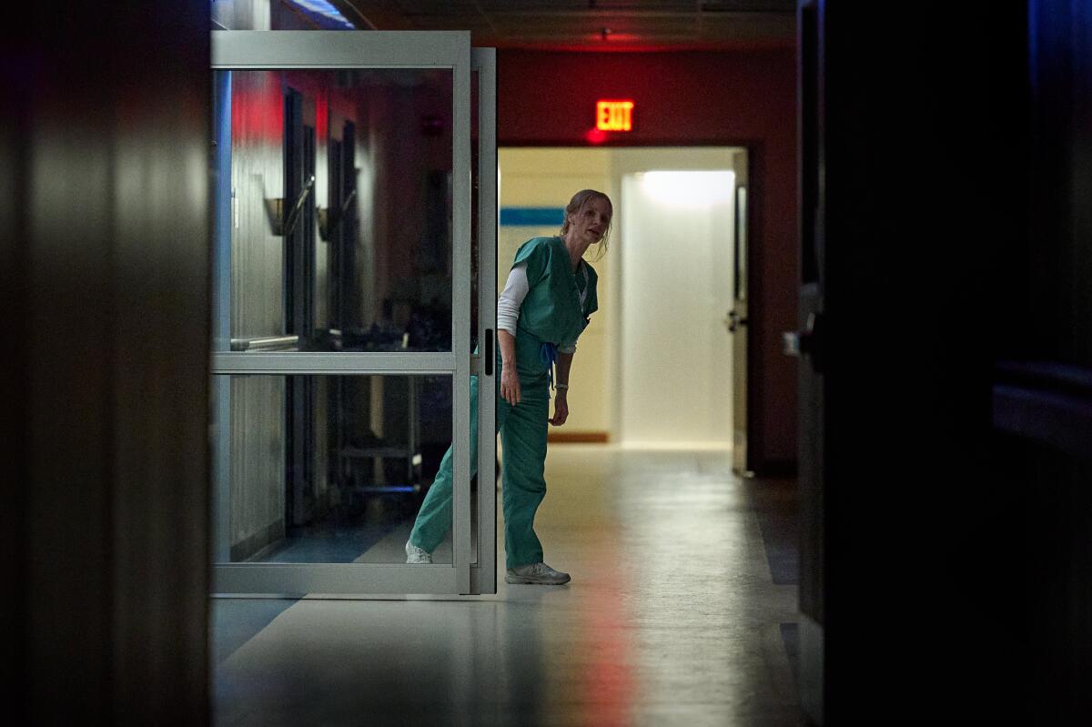 A nurse in scrubs looks down a dark hospital hallway.