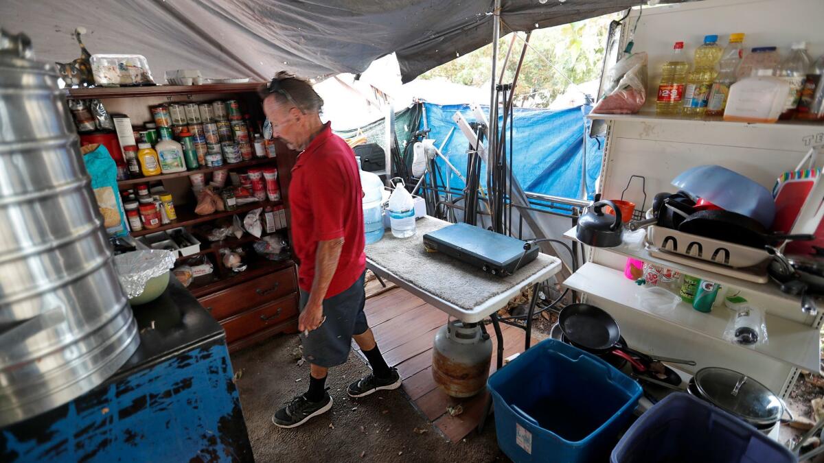 Scott West, 55, who has been homeless for five years, opens his pantry inside his tent compound along the Santa Ana River Trail next to Anaheim Stadium.