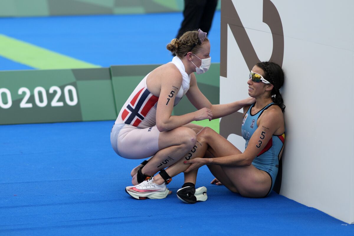 FILE - In this July 27, 2021, file photo, Claire Michel of Belgium is assisted by Lotte Miller of Norway after the finish of the women's individual triathlon competition at the 2020 Summer Olympics, in Tokyo, Japan. In an extraordinary Olympic Games where mental health has been front and center, acts of kindness are everywhere. The world’s most competitive athletes have been captured showing gentleness and warmth to one another — celebrating, pep-talking, wiping away each another’s tears of disappointment. (AP Photo/David Goldman, File)