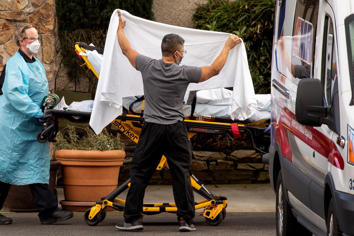 A healthcare worker lifts a white sheet over a person on a stretcher being wheeled to an ambulance