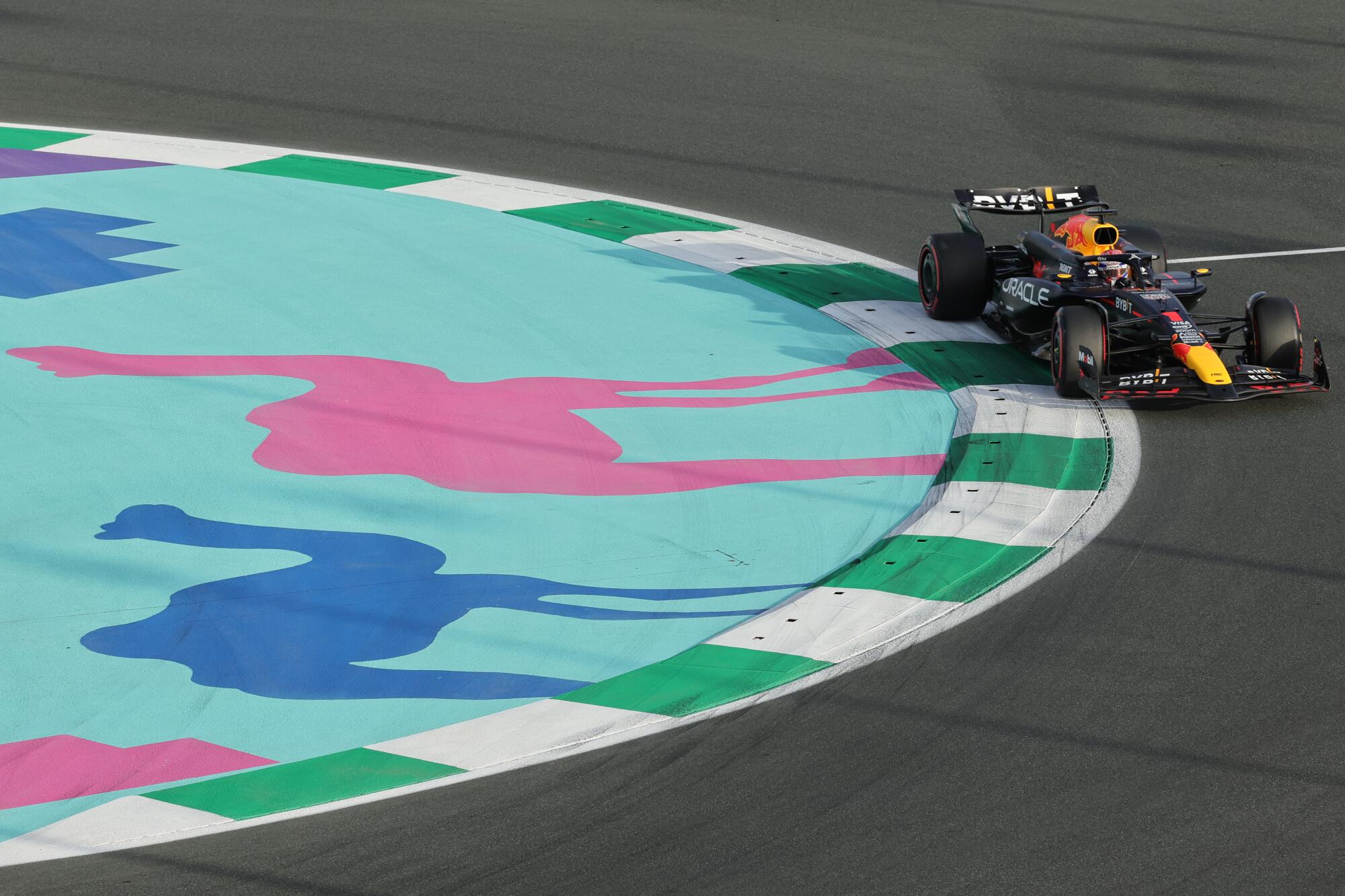 A Formula One race car akes a curve near pink and blue illustrations of camels on a racetrack in Jeddah, Saudi Arabia. 