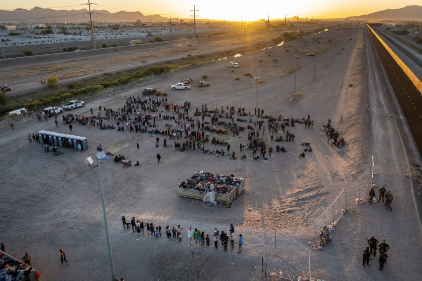 As the sun sets, migrants wait outside a gate in the border fence to enter into El Paso, Texas, to be processed by the Border Patrol, Thursday, May 11, 2023. Migrants rushed across the Mexico border, racing to enter the U.S. before pandemic-related asylum restrictions are lifted in a shift that threatens to put a historic strain on the nation's beleaguered immigration system. (AP Photo/Andres Leighton)