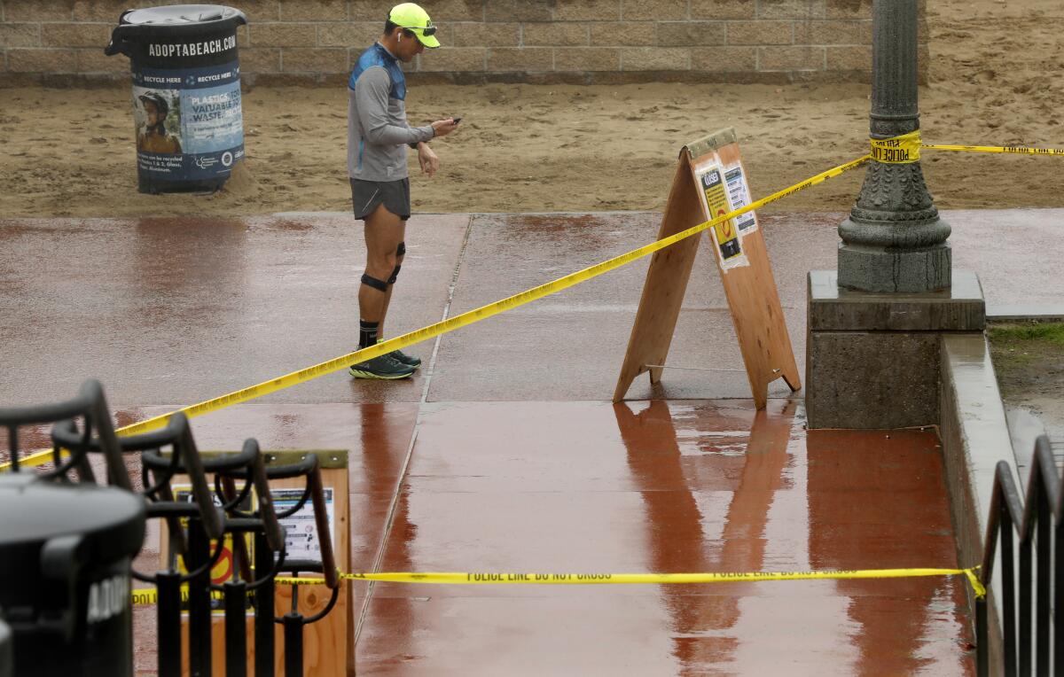 A runner pauses near a taped off staircase leading to the closed Huntington Beach Pier
