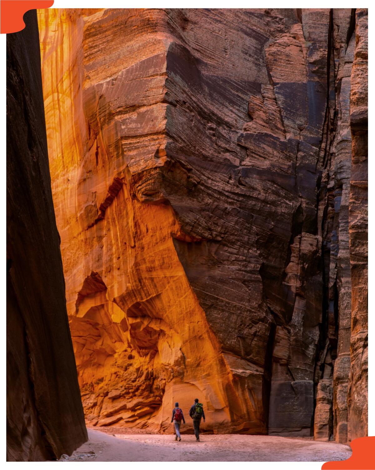 Hikers walk along a sandy trail flanked by the massive sandstone walls of Buckskin Gulch in Utah.